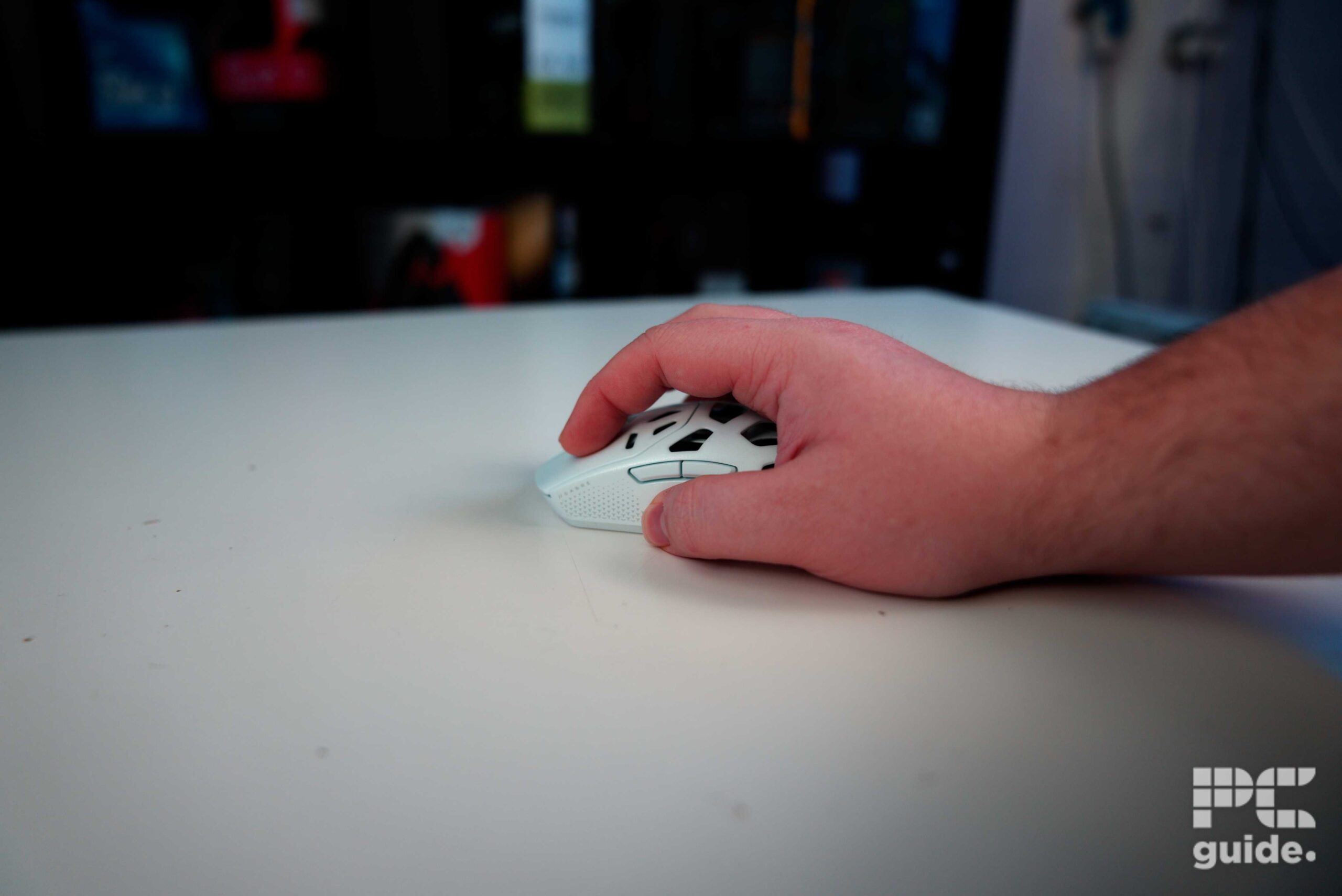 The white Corsair Sabre v2 PRO Wireless MG sitting on a table with a hand resting n it.