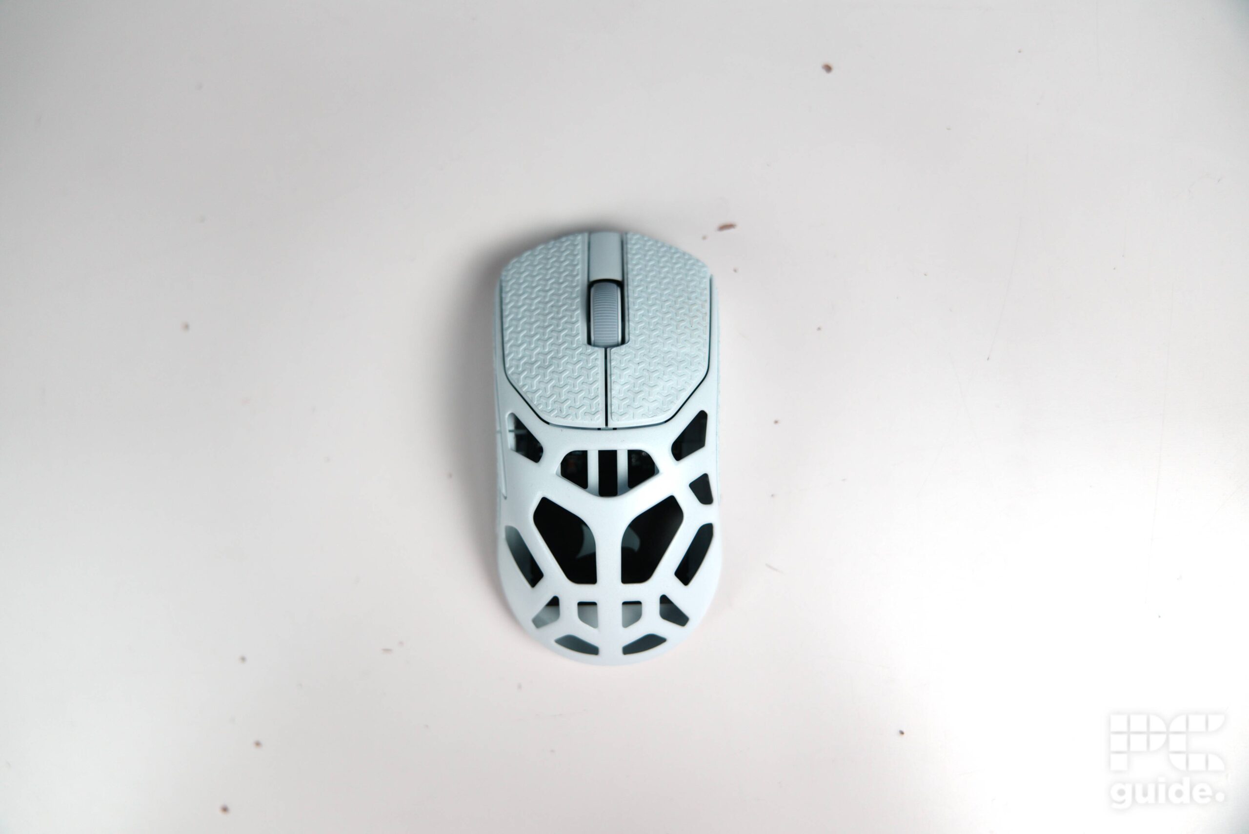 A top down shot of the white Corsair Sabre v2 PRO Wireless MG sitting on a white table. It shows the scroll, clickers, and holey body.
